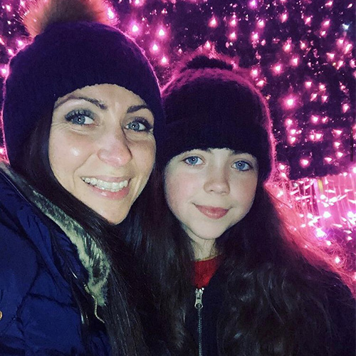 Zoe Mole and daughter standing in front of pink Christmas lights and wearing wooley hats