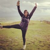 Slimming World member wearing a purple coat and leggings does a star jump in a field