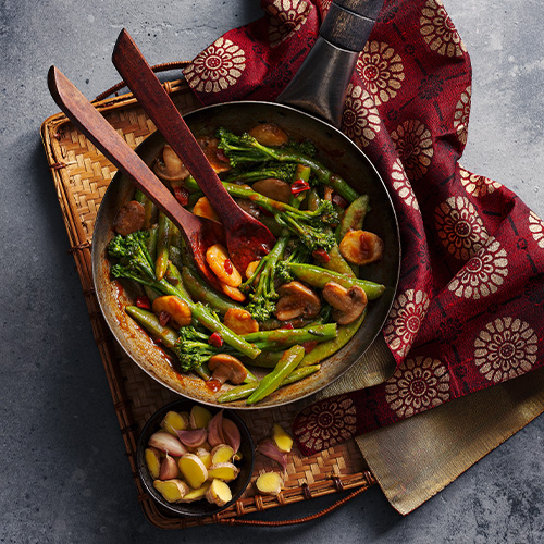 Slimming World food range soy ginger and garlic veg in a black frying pan on a wooden chopping board placed on a grey table.