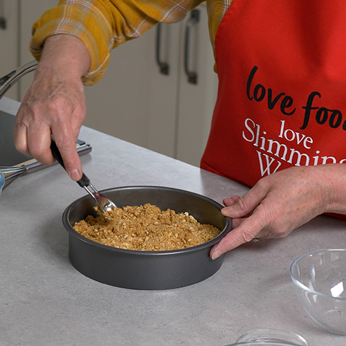 A Slimming World chef smooths the base of a shortbread cheesecake with a spoon