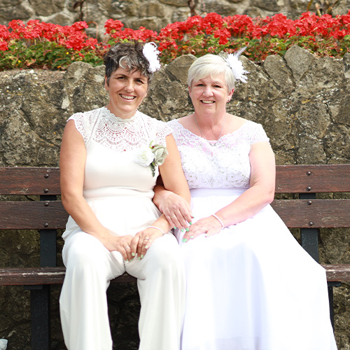Alex newams and wife on their wedding day, sitting on a bench