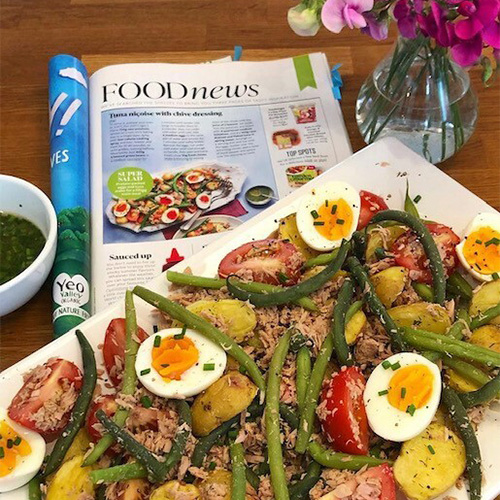 A tuna nicoise salad on a white plate with a copy of Slimming World Magazine in background
