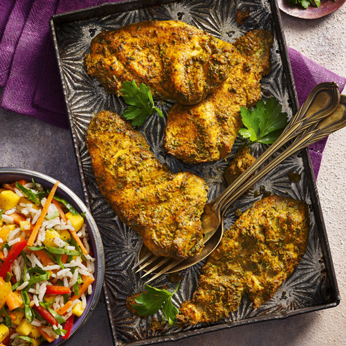 Slimming World coronation chicken escalopes on a grey baking tray on a purple background