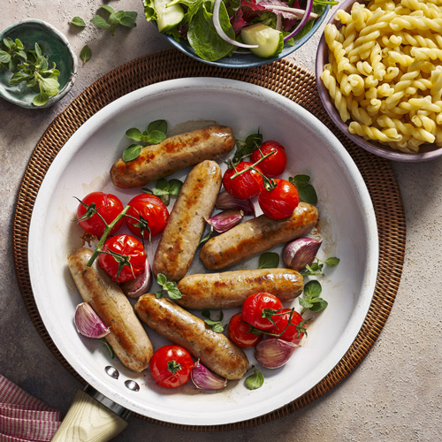 Slimming World Italian-style sausages in a white pan with tomatoes and garlic cloves