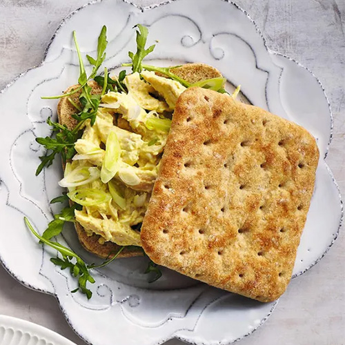Slimming World Coronation chicken sandwich. The sandwich is served on a white plate with a floral design. The background is light gray.