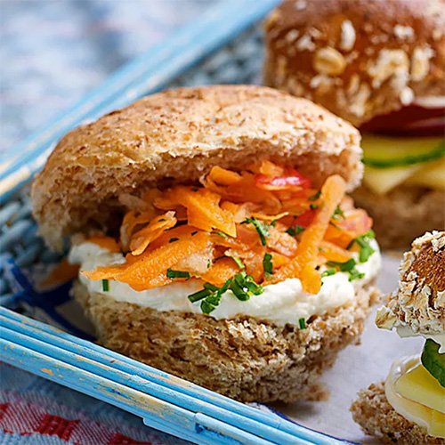 Slimming World Fruity slaw sandwich.  The sandwich consists of a wholemeal roll filled with quark and carrots.  The sandwich sits in a light blue basket placed on a white tablecloth.