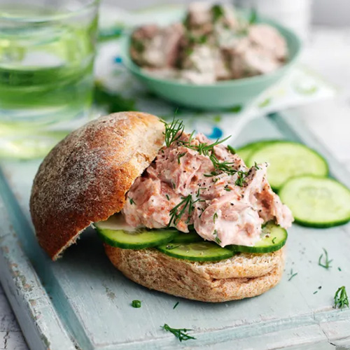 Slimming World Tuna Mari Rose and Cucumber Sandwich. The sandwich is made from a wholemeal roll, cucumber slices and tuna. It sits on a light blue cutting board.