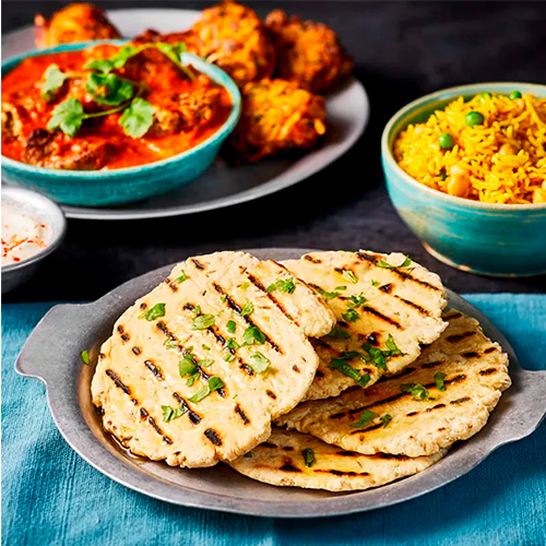 Slimming World naan breads on a grey plate with a blue napkin underneath. Surrounded by an assortment of other dishes.