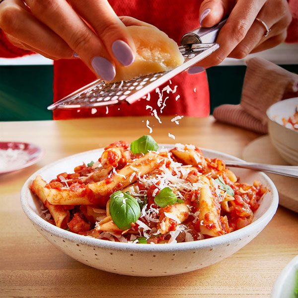 A bowl of pasta in tomato sauce with grated cheese on top